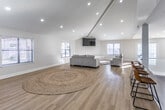 This single-story leasing center in Memphis, Tennessee offers a thoughtfully designed, open-concept interior that blends functionality with modern aesthetics. The main gathering area features soaring vaulted ceilings with exposed beams and recessed lighting, creating a bright and welcoming atmosphere. Light hardwood flooring flows seamlessly throughout the entire space, unifying each area with a clean, contemporary feel. Large windows allow abundant natural light to fill the rooms, while French doors provide additional access points and outdoor views.

The expansive kitchen is a standout feature, showcasing crisp white cabinetry, a generous island with quartz countertops and bar seating, stainless steel appliances, and a built-in cooktop — making it well-suited for hosting and resident engagement events. The kitchen opens directly into the lounge area, which is furnished with comfortable seating, a wall-mounted television, and a woven area rug that adds warmth to the space.

A dedicated private office area, accessible via French doors, provides a quiet workspace with ample room for staff and prospective residents to meet. Additional flex space with clean, neutral walls and recessed lighting rounds out the layout, offering versatility for various leasing and community functions. Overall, the space presents a polished, inviting environment ideal for welcoming future residents.