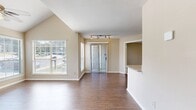 This well-appointed 680 square foot, single-floor unit offers 2 bedrooms and 2 bathrooms with a functional, open layout. The combined kitchen and living room serves as the heart of the home, featuring vaulted ceilings, a ceiling fan, a tile-surround fireplace, and hardwood-style flooring. Large windows and a sliding glass door flood the space with natural light and offer outdoor views. Track lighting and an open-concept pass-through connect the kitchen, which is equipped with stainless steel appliances, warm wood cabinetry, gray countertops, and a double sink. The primary bedroom spans 150 square feet with plush carpeting, a large window, and a sliding double-door closet with direct access to an en-suite bathroom. The second bedroom also features carpet flooring, a window, and a built-in closet organizer with shelving and drawers. Both bathrooms include clean, white finishes, with one featuring tile surround for the tub. The hallway connecting the rooms features hardwood-style flooring, maintaining a cohesive aesthetic throughout this efficiently designed and light-filled residential unit.
