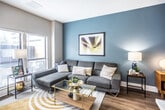 This well-appointed one-bedroom, one-bathroom residence in Memphis, Tennessee offers a thoughtfully designed single-floor layout that maximizes every square foot. The living area makes an immediate impression with its bold teal accent wall, hardwood-style flooring, and large windows that invite natural light and views of the surrounding exterior. A mid-century-inspired credenza and sectional sofa complete the welcoming atmosphere.

The kitchen is a functional standout, featuring two-tone cabinetry with charcoal lower cabinets and white upper cabinets, stainless steel appliances including a gas range, microwave, and refrigerator, and a light quartz countertop peninsula with a built-in sink. A herringbone tile backsplash adds a refined design detail.

The bedroom is a calm retreat with warm neutral and gray tones, hardwood-style flooring, and a drop ceiling with recessed lighting. A skylight window brings in additional natural light, enhancing the room's welcoming feel.

The full bathroom is clean and practical, offering tile flooring, a dark vanity with a sink and mirror, and a shower-tub combination. The overall design of the unit balances modern aesthetics with everyday functionality, creating a comfortable and visually cohesive living space.