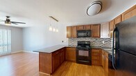 This well-appointed one-bedroom, two-bathroom residence offers a practical and cohesive single-floor layout. The open-concept kitchen and living area serves as the heart of the home, featuring warm honey-toned cabinetry, dark granite countertops, and a peninsula that doubles as a casual dining or workspace. A mosaic tile backsplash adds a decorative touch, while black appliances — including a refrigerator, range, built-in microwave, and dishwasher — provide a unified, contemporary look. Pendant lighting over the peninsula and a flush-mount ceiling fixture illuminate the space effectively. Hardwood-style flooring flows throughout the main living areas, complementing the light, neutral wall tones.

The living area is spacious and bright, anchored by a ceiling fan and large sliding glass doors fitted with vertical blinds that invite natural light and outdoor views. The bedroom features plush carpeting, a built-in closet with louvered doors, and a window with vertical blinds. An additional carpeted room with a window offers flexible use as a secondary bedroom or office.

Both bathrooms are finished with large-format tile and include a tub/shower combination with a decorative mosaic border. One bathroom conveniently houses an in-unit washer, adding everyday practicality. A built-in shelving unit near the entryway provides additional storage.