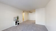 This single-floor residence offers a clean, neutral aesthetic with a practical and comfortable layout. The living area is generously proportioned, featuring plush wall-to-wall carpeting, a ceiling fan with light fixture, and a textured ceiling. A large window near the front entry fills the space with natural light and provides views of mature outdoor greenery, creating a welcoming atmosphere. The layout flows seamlessly from the living area toward the rest of the unit.

The kitchen is efficiently designed with white cabinetry, light-toned countertops, and wood-look vinyl flooring. It is equipped with an electric range and oven, a refrigerator, and an overhead ventilation hood, making it a fully functional cooking space.

Two carpeted bedrooms offer comfortable retreats. One bedroom features a walk-in closet with built-in shelving, providing ample storage. Both rooms are bathed in natural light through windows that overlook the surrounding greenery, and the textured ceilings lend a consistent finish throughout.

The full bathroom is neatly appointed with a tub-shower combination framed by white tile, a single-sink vanity with white cabinetry, a framed mirror, and light wood-look flooring. The overall design of this space emphasizes clean lines, practical functionality, and a bright, airy ambiance.