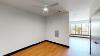 Located at 330 S Shelby Street in downtown Louisville, Kentucky, this efficiently designed single-floor unit offers a thoughtful layout across its living room, kitchen, bathroom, laundry, and utility areas. Warm-toned hardwood-style flooring flows throughout the main living spaces, complementing the clean white walls and bold dark baseboards that define the interior aesthetic.

The open living area is bright and airy, anchored by a ceiling fan with integrated lighting and floor-to-ceiling windows that flood the space with natural light and offer views of the surrounding Louisville cityscape and treetops. An electrical panel is neatly recessed into the wall, keeping the space uncluttered.

The kitchen is well-appointed with warm wood cabinetry, white subway tile backsplash, recessed lighting, and a full suite of stainless steel appliances including a refrigerator, dishwasher, and range. Ample upper and lower cabinet storage makes the kitchen highly functional.

The bathroom features a striking design with large dark hexagonal floor tiles, matte black fixtures and grab bars, a soaking tub with a handheld shower, and a wood-toned vanity topped with a white sink and a framed mirror flanked by wall sconces. A dedicated laundry area and utility room round out the unit's practical amenities.