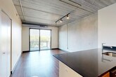 Located at 618 South Main Street in the heart of Ann Arbor, this one-bedroom, one-bathroom urban loft showcases an industrial-modern aesthetic throughout. The open-concept living and kitchen area serves as the centerpiece of the space, featuring striking exposed concrete ceilings with visible ductwork and track lighting that reinforce the loft's character. Rich hardwood flooring runs throughout the main living areas, complementing the kitchen's sleek dark granite countertops, warm wood cabinetry, stainless steel appliances, and a peninsula with an integrated sink — ideal for both cooking and entertaining. Floor-to-ceiling sliding glass doors flood the living area with natural light and provide access to a private balcony with lush outdoor views. The bedroom continues the industrial aesthetic with an exposed concrete ceiling, plush carpet flooring, a dedicated closet, and its own sliding glass door to the balcony, offering a serene retreat. The bathroom features matching wood cabinetry with dark granite countertops, a large vanity mirror, and hardwood-style flooring, maintaining design consistency across the unit. A dedicated closet provides additional storage. This well-appointed loft offers a compelling blend of urban industrial design and modern comfort in a prime Ann Arbor location.
