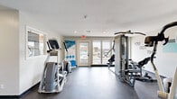 Located in North Richland Hills, TX, this dedicated fitness center offers a well-equipped exercise space designed to support a range of workout routines. The room features durable dark flooring throughout, providing a practical and clean surface suited for high-traffic use.

Natural light pours in through multiple large windows along the walls, offering views of the surrounding area and creating an open, energizing atmosphere. The bright white walls are accented with bold motivational typography, reinforcing the gym's active and encouraging ambiance.

The space is outfitted with a variety of exercise equipment, including treadmills, elliptical machines, a multi-station cable weight system, and a rowing/functional trainer bench. A stability ball and a metal shelving unit storing free weights and accessories provide additional workout versatility. A wall-mounted flat-screen television adds entertainment for those logging time on cardio machines.

Access is provided through a modern steel-framed glass door, contributing to the space's contemporary aesthetic. Recessed lighting supplements the abundant natural light, ensuring the room remains well-lit throughout the day. A secondary door offers an additional entry and exit point. The overall design is clean, functional, and purposefully arranged to maximize the use of the available floor area.