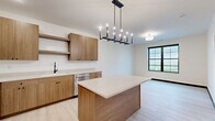 Located at 300 Anthem Dr in Huxley, Iowa, this thoughtfully designed 1-bedroom, 2-bathroom unit offers a clean, modern aesthetic across a single floor. Light-toned luxury vinyl plank flooring runs throughout, complemented by bold black door frames and baseboards that create a striking contemporary contrast against crisp white walls.

The open-concept kitchen and dining area serves as the heart of the unit, featuring flat-panel wood-toned cabinetry, white quartz countertops, a center island, stainless steel appliances including a refrigerator, range, microwave, and dishwasher, and a matte black faucet. Recessed lighting and a pendant chandelier over the island add warmth and functionality to the space.

The bedroom is a comfortable, well-proportioned room bathed in natural light through a large grid-pane window that frames outdoor views. The space is finished with the same light flooring and neutral walls found throughout the unit.

Two bathrooms provide added convenience, with one featuring a walk-in shower, white vanity, and matte black hardware accents. A utility area with a stacked washer and dryer offers in-unit laundry. The overall design is modern, minimal, and move-in ready, making efficient use of every square foot.