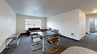 Located at 1260 Ferry St in Eugene, Oregon, this single-floor, three-bedroom, two-bathroom unit offers a practical and efficiently designed layout. The open living and dining area serves as the heart of the home, featuring dark carpeting, neutral white walls, and a textured ceiling. A built-in cabinet unit along one wall provides additional storage, while windows allow natural light to brighten the shared space. Adjacent to the living area, the kitchen is compact and functional, offering essential workspace and cabinetry with a modern finish. The three bedrooms are clean and straightforward, each featuring dark carpet, white walls, and windows that bring in natural light. The primary bedroom offers a bit more space, while the secondary bedrooms are well-suited for single occupancy. Each room includes closet access, and the unit features a total of four closets for ample storage. The two bathrooms are finished with gray tile-patterned flooring, dark countertops, and marble-style wall panels, with one bathroom featuring a window with outdoor views. A dedicated laundry room and two hallways connecting the spaces round out this well-organized, no-frills unit.