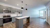 Located at 2223 Lee Rd in Cleveland Heights, Ohio, this thoughtfully designed one-bedroom, one-bathroom residence offers a clean, modern aesthetic across a single floor. The open-concept layout connects the kitchen and living area seamlessly, creating a bright, airy atmosphere ideal for both everyday living and entertaining. The kitchen is a standout feature, boasting gray shaker-style cabinetry, crisp white quartz countertops, a white subway tile backsplash, and a full suite of stainless steel appliances including a refrigerator, range, and microwave. A central island with a striking blue accent base and pendant lighting overhead adds both function and visual interest. Durable wood-look flooring runs throughout the main living areas, complementing the neutral white walls and recessed lighting. The living area benefits from natural light through large windows and a glass-panel entry door. The bedroom is carpeted for comfort and features a walk-in closet with built-in shelving, providing ample storage. The bathroom is finished with matching gray cabinetry, a white vanity countertop, a walk-in shower with glass enclosure, and the same warm wood-look flooring for a cohesive look.