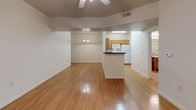 This single-floor residence offers a well-designed, open-concept layout that seamlessly connects the main living areas. The combined living and dining space is highlighted by warm hardwood-style flooring that runs throughout, a decorative chandelier over the dining area, and a ceiling fan in the living room. A wall of vertical blinds leads to what appears to be an outdoor access point, allowing natural light to filter into the space. A half-wall peninsula separates the kitchen from the main living area, providing both visual connectivity and functional counter space. The kitchen is equipped with honey-toned wood cabinetry, dark granite-style countertops, and white appliances including a range, over-the-range microwave, and refrigerator. Two bedrooms are finished with plush wall-to-wall carpeting, ceiling fans with light fixtures, and windows fitted with blinds. One bedroom includes a closet with paneled doors. Both bathrooms feature tile flooring, warm wood vanity cabinetry, granite-style countertops, and large mirrors. One bathroom offers a shower/tub combo, while the other includes accessible grab bars and a separate shower area, catering to a range of accessibility needs. The overall ambiance is clean, functional, and welcoming.