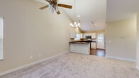This two-floor home is defined by its dramatic vaulted ceilings in the main living area, creating an expansive, airy atmosphere. The open-concept layout seamlessly connects the living room and kitchen, where soft carpet transitions to hardwood-style flooring. A ceiling fan and elegant chandelier hang above, complemented by track lighting and recessed fixtures that illuminate the space effectively.

The kitchen features white cabinetry with dark granite countertops, a peninsula that doubles as a breakfast bar, a stainless steel appliance suite, and a window above the sink that brings in natural light. A secondary exterior door provides additional access.

The bedrooms are carpeted and well-proportioned, each equipped with ceiling fans and windows offering outdoor views. The primary bedroom includes a generous walk-in closet with built-in shelving and double hanging rods. A full bathroom serves the home with a tub/shower combination, white cabinetry with granite countertops, and wood-look flooring.

Additional features include a narrow utility corridor with tile flooring and a baseboard heater, adding functional utility to the home's overall layout. Warm neutral tones throughout create a cohesive and welcoming ambiance.
