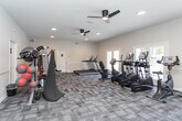 Located at 3822 Mizell Rd in Greensboro, NC, this fitness center is a well-appointed, single-floor facility designed to support a wide range of workout routines. The space is generously sized, offering an open layout that comfortably accommodates multiple exercise zones without feeling crowded.

The flooring throughout consists of patterned, multi-tone carpet tiles that provide both comfort and durability underfoot. Recessed lighting and ceiling fans are installed throughout, ensuring the space remains well-lit and well-ventilated during workouts.

Along one side of the facility, a row of cardio equipment — including treadmills, elliptical trainers, and stationary bikes — faces a wall of large French doors and windows that open to views of an outdoor pool area, flooding the space with natural light and providing a refreshing outdoor connection.

The strength training section is equally comprehensive, featuring a cable machine, a Smith machine with a weight bench, a full dumbbell rack with a wide range of weights, and a dedicated functional training station equipped with resistance bands, medicine balls, stability balls, and kettlebells. A curved slant board rounds out the functional fitness options.

The walls are finished in neutral tones with chair-rail detailing, contributing to a clean, polished aesthetic. The overall ambiance is bright, airy, and motivating — a professional-grade fitness environment suited for residents of all fitness levels.