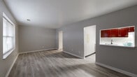 Located at 6847 Greenleaf Dr in Reynoldsburg, Ohio, this single-story, 3-bedroom, 1-bathroom home offers a practical and well-organized layout. The open living and dining area features light-toned luxury vinyl plank flooring and neutral gray walls, creating a clean, modern aesthetic. A pass-through opening connects the living space to the kitchen, which is equipped with rich dark-red cabinetry and a sink, providing a functional cooking area with visual continuity to the main living space. Natural light filters in through windows fitted with blinds throughout the home. A central hallway connects the living area to the three bedrooms, all of which feature wall-to-wall carpet in a warm neutral tone. The generously sized primary bedroom offers ample space and includes a window for natural light. The two additional bedrooms are comfortably sized and well-suited for various uses. The full bathroom features a long vanity with white countertops, dark-stained cabinetry, dual mirrors, and a separate water closet area with a toilet and clothing rod. Two closets provide convenient storage throughout the home. The overall design is cohesive, with consistent neutral tones and clean finishes throughout.