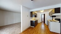 This two-floor residence in Spokane, WA offers a practical and functional layout spread across two connected levels linked by a carpeted staircase with a wood handrail. The main level features a spacious carpeted living room with a sliding glass door that invites natural light and outdoor views. The galley-style kitchen is well-appointed with dark wood cabinetry lining both walls, ample counter space, a double-basin sink, and white appliances including a refrigerator and dishwasher. An adjacent dining area with hardwood-style flooring, a ceiling fan, and a large window provides a bright, open feel. A conveniently located bathroom on this level includes hardwood-style flooring, a vanity with dark cabinetry, and baseboard heating. The upper level hosts additional carpeted bedrooms, each offering windows with views of the surrounding tree-lined landscape and baseboard heating. A full bathroom upstairs features a window for natural light, a vanity with dark cabinetry, a white countertop, and a wall-mounted mirror. Throughout the space, textured ceilings, neutral wall tones, and dark wood door frames create a cohesive and understated aesthetic. Baseboard heating is present throughout, ensuring comfort across both floors.