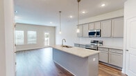 Located at 352 Stately Oaks Court in Hoschton, Georgia, this two-story home offers a well-designed layout spread across two floors. The main level features an open-concept kitchen and living area anchored by a large center island with granite countertops, an undermount sink, and stylish pendant lighting. Gray cabinetry and stainless steel appliances complete the kitchen, which flows seamlessly into the living space. A wall of windows and a glass-panel door fill the living area with natural light and provide access to the outdoors. Warm hardwood-style flooring runs throughout both levels, adding continuity and a modern aesthetic. A clean hallway with a staircase connects the two floors. Upstairs, the generously sized primary bedroom includes a ceiling fan, crown molding, and natural light from a large window. The walk-in closet is equipped with built-in wire shelving. The bathrooms feature granite-topped gray vanities, brushed nickel fixtures, and tub-shower combinations. A dedicated laundry room houses a full-size washer and dryer with overhead shelving for added storage. Three additional bedrooms are bright and well-proportioned, each with natural light. The home's clean, neutral palette creates a cohesive and move-in-ready environment throughout.