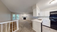 Located at 323 Timber Ridge Dr in Kalamazoo, Michigan, this two-floor residence offers a well-organized layout designed for comfortable everyday living. The main level centers around an open-concept living and kitchen area, where plush carpeting flows through a spacious living room anchored by a classic fireplace. Sliding glass doors lead to an outdoor deck, bringing in natural light and views of surrounding greenery. The kitchen features white cabinetry, light quartz countertops, a peninsula with an undermount sink, and black appliances including a range, built-in microwave, dishwasher, and refrigerator. Light wood-style flooring runs throughout the kitchen, complementing the clean, neutral color palette. A staircase with white railings connects the two floors. The bathrooms are finished with quartz countertops — one featuring a single undermount sink, and another offering a dual-sink vanity with louvered cabinet accents and glass shelving, providing ample storage. The bedrooms are carpeted and well-lit by large windows that frame views of lush outdoor foliage, lending a calm, natural atmosphere throughout. Neutral gray tones, textured ceilings, and consistent finishes give the entire home a cohesive, move-in-ready feel.