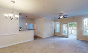This single-floor residence offers a thoughtfully designed open-concept layout that seamlessly connects the living, dining, and kitchen areas. The spacious living room is finished with plush carpet, crown molding, and a ceiling fan with integrated lighting. French doors open directly onto a private balcony, allowing natural light to pour in and providing pleasant outdoor views of surrounding greenery.

The kitchen is a functional highlight, featuring rich cherry-toned cabinetry that extends to the ceiling, granite-look countertops, and a suite of black appliances including a refrigerator, range, and over-the-range microwave. A wraparound breakfast bar provides additional prep and seating space, while a pendant light adds a refined touch overhead. A dedicated dining area adjoins the kitchen, complete with its own ceiling fan and chandelier combination.

The bedrooms are carpeted and bathed in natural light from large windows with blinds. Each room offers generous wall space, and at least one bedroom includes a closet with built-in shelving and hanging rods. The bathroom is finished with large-format tile flooring, a rich wood vanity with light countertops, a wide mirror, and a tub-shower combination equipped with accessibility grab bars. Throughout, warm neutral tones and crown molding details create a cohesive and inviting atmosphere.
