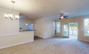 This single-floor residence offers a thoughtfully designed open-concept layout that seamlessly connects the living, dining, and kitchen areas. The spacious living room is finished with plush carpet, crown molding, and a ceiling fan with integrated lighting. French doors open directly onto a private balcony, allowing natural light to pour in and providing pleasant outdoor views of surrounding greenery.

The kitchen is a functional highlight, featuring rich cherry-toned cabinetry that extends to the ceiling, granite-look countertops, and a suite of black appliances including a refrigerator, range, and over-the-range microwave. A wraparound breakfast bar provides additional prep and seating space, while a pendant light adds a refined touch overhead. A dedicated dining area adjoins the kitchen, complete with its own ceiling fan and chandelier combination.

The bedrooms are carpeted and bathed in natural light from large windows with blinds. Each room offers generous wall space, and at least one bedroom includes a closet with built-in shelving and hanging rods. The bathroom is finished with large-format tile flooring, a rich wood vanity with light countertops, a wide mirror, and a tub-shower combination equipped with accessibility grab bars. Throughout, warm neutral tones and crown molding details create a cohesive and inviting atmosphere.