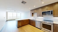 Located in the heart of downtown Dallas on Pacific Ave, this contemporary high-rise residence offers one bedroom, two bathrooms, and a thoughtfully designed open-concept layout. Floor-to-ceiling windows in both the living area and bedroom flood the space with natural light and frame breathtaking panoramic views of the Dallas skyline and surrounding cityscape.

The combined kitchen and living room serves as the central hub of the unit. The kitchen features warm wood-toned cabinetry extending to the ceiling, stainless steel appliances including a range, dishwasher, and built-in microwave, white countertops, and a classic tile backsplash. Light hardwood-style flooring flows through the main living areas, complemented by recessed lighting and a clean, modern palette.

The spacious primary bedroom is finished with plush carpeting, a ceiling fan, and expansive windows that continue the stunning city views. It connects to a dedicated walk-in closet with built-in shelving and hanging rails. The primary bathroom offers a refined aesthetic with wood-grain cabinetry, gold-toned hardware, a large framed mirror, and elegant tile flooring. An in-unit laundry area houses a full-size Whirlpool washer and dryer. The overall ambiance is sleek, bright, and urban.