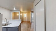 Located in Seattle's University District, this single-floor 2-bedroom unit offers a clean, functional layout designed to maximize every square foot. The main living and entry area welcomes you with light wood-look luxury vinyl plank flooring, neutral gray walls, and a textured ceiling that adds subtle dimension. A wall-mounted sconce near the entry provides warm accent lighting, and a windowed front door allows natural light to filter into the space.

The kitchen is positioned off the main living area and features a practical peninsula that defines the cooking zone from the rest of the floor plan. Dark navy cabinetry contrasts cleanly against white appliances, including a refrigerator and range, while a stainless steel sink completes the setup. Recessed lighting keeps the kitchen bright and functional.

Both bedrooms offer plush carpeting and windows dressed with horizontal blinds that overlook lush greenery, providing a calm, natural backdrop. The primary bedroom includes a wall-mounted light fixture, adding a cozy and well-lit atmosphere. The secondary bedroom is similarly sized with a large window that fills the room with natural light. Neutral tones throughout the unit create a cohesive and move-in-ready aesthetic, ideal for those seeking a no-frills, practical home in a vibrant Seattle neighborhood.