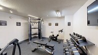 Located at 123 E McCullough Dr in Charlotte, NC, this fitness center offers a well-equipped exercise space designed to support a variety of workout routines. The room features durable speckled rubber flooring throughout, providing a safe and resilient surface for all types of physical activity. Overhead fluorescent and track lighting ensure the space is consistently well-lit, while a textured ceiling adds a clean, functional aesthetic.

The cardio section is outfitted with a treadmill and an elliptical trainer, catering to endurance and low-impact exercise needs. A Matrix-brand spin bike offers an additional option for cycling workouts. Strength training is supported by a multi-functional cable machine complete with a variety of attachments, an adjustable weight bench, and a full rack of dumbbells in graduated weights. A wall-mounted flat-screen television provides entertainment during workouts.

Motivational signage bearing words such as "Hustle," "Grit," "Success," and "Execute" is displayed throughout the room, contributing to an energizing atmosphere. The space is clean, organized, and efficiently arranged to maximize usability within its compact footprint, making it a practical amenity for residents or guests at this Charlotte location.