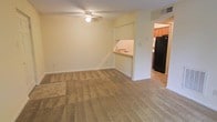 This single-floor residence offers a straightforward and functional layout designed for comfortable everyday living. The main living area is spacious and open, finished with wall-to-wall carpeting in a neutral beige tone that creates a warm and inviting atmosphere. A ceiling fan is centrally positioned overhead, providing both practicality and subtle visual interest to the room. Soft, light-colored walls throughout contribute to a bright and airy feel.

The living space flows seamlessly toward the kitchen, which is accessible via an open pass-through counter with a built-in sink — a design detail that maintains a sense of openness between the two areas while defining each space. The kitchen features warm-toned wooden cabinetry, tile flooring, and a full-size black refrigerator, offering a functional cooking and food preparation environment. Additional counter space and cabinetry provide ample storage. A HVAC vent is visible in the ceiling, ensuring year-round climate control throughout the home. The overall design is clean and understated, with a neutral color scheme that offers a versatile canvas for personalization.