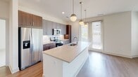 This single-floor residence presents a thoughtfully designed layout with modern finishes and a clean, contemporary aesthetic. The open-concept kitchen serves as a central highlight, featuring a large island with a light quartz countertop, an undermount sink, and globe pendant lighting. Cabinetry combines gray shaker-style uppers with rich walnut-toned lower cabinets, complemented by a marble-look tile backsplash and a full suite of stainless steel appliances. Light wood-look flooring runs throughout the kitchen and connects seamlessly to a generous living area, where large windows invite abundant natural light and a ceiling fan adds functional comfort.

The bedrooms are carpeted and well-proportioned, each featuring windows with blinds that frame views of surrounding greenery. One bedroom benefits from a ceiling fan and an especially bright, airy feel. The hallway connecting the rooms is clean and efficient, with louvered closet doors adding a classic detail.

The bathrooms are finished with large-format marble-look tile flooring and a tub-shower combination featuring matching tile surround. The vanity area includes dark walnut cabinetry, a framed mirror, and a well-lit wall sconce, creating a polished, functional space throughout.