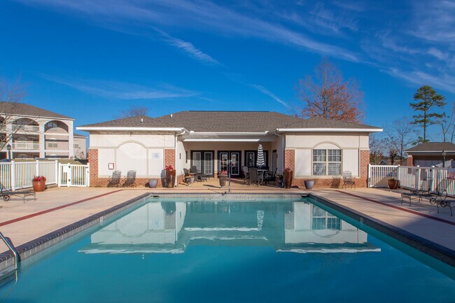 Vista a nivel del suelo de la piscina con agua tranquila, la terraza circundante con asientos y la casa club con patio cubierto y entrada. - Parham Pointe