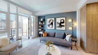 Located in the heart of downtown Los Angeles, this modern single-floor residence at 825 S Hill St offers a refined urban living experience with thoughtfully designed interiors and high-quality finishes throughout. The open-plan living area serves as the centerpiece of the home, anchored by a bold blue feature wall adorned with large-scale abstract artwork. Light tile flooring, recessed lighting, and access to an outdoor balcony with sweeping city skyline views create a bright and airy ambiance. The kitchen is outfitted with sleek high-gloss white upper cabinetry, warm wood-toned lower cabinets, quartz countertops, stainless steel appliances including a gas cooktop and built-in oven, and an undermount sink — all framing a clean, functional workspace. The primary bedroom enjoys floor-to-ceiling windows and direct balcony access, flooding the room with natural light and offering panoramic downtown views, complemented by a ceiling fan. A secondary bedroom features deep charcoal walls for a moody, intimate atmosphere. Both bathrooms are finished with large-format beige stone tiles, soaking tubs with integrated shower fixtures, floating wood vanities, and expansive mirrors, delivering a spa-like aesthetic throughout.