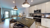 Located in Jacksonville, FL (32207), this thoughtfully designed single-floor residence combines modern finishes with a warm, coastal-inspired aesthetic. The open-concept kitchen is a standout feature, showcasing crisp white shaker cabinetry extending to the ceiling, dark granite countertops, and a full suite of stainless steel appliances including a refrigerator, range, microwave, and dishwasher. A generously sized kitchen island with matching granite and an undermount sink serves as both a prep space and a casual dining area, illuminated by stylish pendant lighting. Light wood-tone flooring flows seamlessly throughout the space, connecting the kitchen to the living area. The living room is bright and inviting, benefiting from natural light through large windows with blinds and sheer curtains, and includes access to a private balcony. The bedroom is comfortably proportioned, featuring the same light hardwood flooring, dual windows for ample natural light, and a serene, neutral palette. The bathroom is well-equipped with white cabinetry, dark granite countertops, an undermount sink, and a full tub-shower combination with clean white tile surround. Recessed lighting and a consistent soft gray color scheme throughout lend the home a cohesive, contemporary feel.