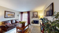 Located at 8061 Wood Scape Dr in Charlotte, NC, this well-appointed single-floor residence offers a thoughtfully designed layout with a warm, cohesive aesthetic throughout. The living room serves as the heart of the home, showcasing light wood-style flooring, a classic white fireplace as the focal point, and a sliding glass door framed by rich burgundy drapes that invite natural light. The space comfortably accommodates a full seating arrangement anchored by a patterned area rug. Adjacent to the living area, the dining room features a pendant light fixture centered over a round wood dining table, complemented by a large framed mirror and neutral warm-toned walls with chair-rail detailing. The kitchen is outfitted with dark espresso cabinetry, granite-style countertops, and black appliances, offering a sleek and functional cooking space. The bedroom provides a serene retreat with plush carpeting, a large window allowing natural light, and ample space for a full bedroom suite. The bathroom includes a generous granite vanity counter with dark wood cabinetry, a well-lit mirror, and a built-in vanity seating area—combining practicality with an elegant finish. Throughout the home, consistent flooring, neutral tones, and warm lighting create a cohesive and inviting atmosphere.