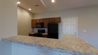 Located at 2066 Home Road in Grove City, Ohio, this single-story property offers a practical and well-appointed layout designed for comfortable everyday living. The kitchen serves as a central feature of the space, showcasing an extended granite-style countertop that provides generous prep and serving space while also functioning as a natural room divider, creating an open-concept feel. Warm-toned wood cabinetry lines the kitchen walls, offering ample upper storage, and is complemented by a full suite of black appliances including a range with overhead microwave and a full-size refrigerator. Recessed lighting illuminates the kitchen area, contributing to a clean, functional atmosphere. The neutral wall tones throughout create a versatile backdrop suitable for a variety of interior styles. A paneled door visible from the kitchen suggests convenient access to an adjacent room or utility area. The single-floor layout promotes ease of movement throughout the home, making it an accessible and efficient living space. Overall, the property presents a tidy, move-in ready environment in an established Grove City neighborhood.