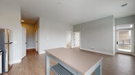 Located at 750 E Broad St in Columbus, Ohio, this single-floor residence offers a thoughtfully designed layout with modern finishes and a clean, contemporary aesthetic. The open-concept kitchen and living area form the heart of the space, anchored by a well-appointed kitchen featuring two-tone cabinetry — white uppers paired with gray lowers — complemented by taupe quartz countertops, a white subway tile backsplash, stainless steel appliances, and a matte black double-basin sink. A built-in wine rack cabinet and pendant lighting add refined detail. The adjoining living and dining area is bathed in natural light through multiple windows with city views, and features light-toned wood-look flooring that flows throughout the main living spaces. The bedrooms are carpeted for comfort and offer generous closet space, with large windows framing views of the Columbus skyline. White interior doors with matte black hardware provide a consistent modern design language throughout. The bathroom stands out with a bold teal accent wall, light wood-tone flooring, and a white vanity with dark countertop and black fixtures. The overall palette of cool grays, crisp whites, and accent tones creates a cohesive, contemporary living environment.