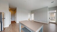 Located at 750 E Broad St in Columbus, Ohio, this single-floor residence offers a thoughtfully designed layout with modern finishes and a clean, contemporary aesthetic. The open-concept kitchen and living area form the heart of the space, anchored by a well-appointed kitchen featuring two-tone cabinetry — white uppers paired with gray lowers — complemented by taupe quartz countertops, a white subway tile backsplash, stainless steel appliances, and a matte black double-basin sink. A built-in wine rack cabinet and pendant lighting add refined detail. The adjoining living and dining area is bathed in natural light through multiple windows with city views, and features light-toned wood-look flooring that flows throughout the main living spaces. The bedrooms are carpeted for comfort and offer generous closet space, with large windows framing views of the Columbus skyline. White interior doors with matte black hardware provide a consistent modern design language throughout. The bathroom stands out with a bold teal accent wall, light wood-tone flooring, and a white vanity with dark countertop and black fixtures. The overall palette of cool grays, crisp whites, and accent tones creates a cohesive, contemporary living environment.