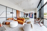 Located at 110 Somerville Ave in Chattanooga's North Shore neighborhood, this single-floor space showcases a compelling blend of industrial character and contemporary design. The layout is open and expansive, with soaring ceilings that amplify the sense of volume throughout. Exposed white ductwork runs overhead, complementing the industrial aesthetic while maintaining a clean, polished look.

A defining architectural feature is the steel-framed frosted glass partition wall, which adds visual structure to the living area without sacrificing openness. Adjacent exposed brick walls provide warmth and texture, grounding the modern design with historic character. The living area is anchored by a generous cognac leather sectional, a round upholstered ottoman, and a wall-mounted flat-screen TV, creating a comfortable and stylish lounge environment.

The open kitchen is outfitted with dark wood cabinetry extending to the ceiling, white quartz countertops, stainless steel appliances including a French-door refrigerator, and an induction cooktop. A kitchen island with bar seating provides an additional gathering point. A dining area with a light wood table and green chairs connects seamlessly to the kitchen and living zones. Bold wall art adds a vibrant focal point to the space, enhancing its curated, contemporary ambiance.