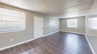 Located at 2401 Jammes Rd in Jacksonville, Florida, this single-floor, 2-bedroom, 1-bathroom residence offers a practical and comfortable layout. The interior is finished with consistent wood-style laminate flooring throughout, complemented by neutral gray walls and white baseboards that create a clean, cohesive look. Textured ceilings add a classic touch to each room.

The main living area is an open, well-lit space featuring two windows that allow ample natural light and views of the surrounding area. A six-panel entry door anchors the front of the space. Both bedrooms are generously sized, each with windows fitted with blinds for privacy and natural light control. The primary bedroom includes a louvered bi-fold closet door, while the second bedroom benefits from a dedicated walk-in closet with built-in wire shelving and hanging rods for organized storage.

The bathroom is outfitted with a full tub-and-shower combination featuring white tile surrounds and safety grab bars, along with standard fixtures. A hallway connects the main rooms and includes a utility panel. The kitchen area, visible in the floor plan, rounds out the functional layout of this straightforward and well-maintained residence.