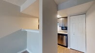 This single-floor space offers a thoughtfully designed layout that balances functionality and comfort. The kitchen is a standout feature, showcasing dark gray cabinetry with sleek hardware, light quartz countertops, and a classic white subway tile backsplash. Stainless steel appliances — including a refrigerator, dishwasher, and built-in microwave — are complemented by warm wood-look flooring that runs throughout the space. A structural column near the kitchen entry adds architectural character while defining the transition between living and cooking areas. The open living area is bright and welcoming, featuring durable wood-look flooring, neutral gray walls, and a textured ceiling. Large sliding glass doors frame a view of the lush outdoor greenery, flooding the room with natural light and providing easy access to the exterior. The bathroom is clean and functional, featuring a full-size soaking tub with a white tiled surround, a toilet, and warm-toned walls. The overall design palette is neutral and contemporary, with consistent flooring and finishes throughout that create a cohesive and move-in-ready environment.