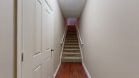 This two-floor residence offers a well-organized layout designed for comfortable everyday living. The main level features rich hardwood flooring throughout the entryway and staircase corridor, where a carpeted staircase with a white-painted handrail connects the two floors. The kitchen is a functional centerpiece, showcasing warm cherry wood cabinetry, granite countertops, stainless steel appliances including a refrigerator, microwave, and range, and a peninsula that opens toward the living area. Crown molding accents the main living space, which is finished with plush carpeting and French doors that allow natural light to flow in while providing access to an outdoor balcony with exterior views. A built-in desk nook adjacent to the kitchen adds a practical workspace element. The upper level features a generously sized open loft area with carpet flooring and a ceiling fan, overlooking the lower level through a half-wall railing. The primary bathroom is well-appointed with a lengthy dual-sink vanity featuring rich wood cabinetry, light stone-style tile flooring, a large mirror, and accessibility-friendly grab bars. Additional bedrooms are carpeted and bright with neutral walls. A spacious walk-in closet with wire shelving systems provides ample storage. The space is finished throughout in warm neutral tones, creating a cohesive and inviting atmosphere.