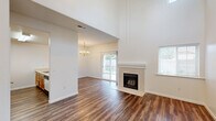 Located at 2300 Riverview Drive in Madera, CA, this two-story, three-bedroom, two-bathroom home offers a well-organized layout across two floors. The main level provides generous living space, highlighted by a soaring vaulted ceiling in the living room that creates an airy, open atmosphere. A tile-surround fireplace serves as the focal point of the living area, complemented by rich hardwood-style flooring that extends throughout the main level. Sliding glass doors lead directly to a covered patio, offering a seamless indoor-outdoor connection with views of the surrounding greenery. The combined dining room and kitchen area features a peninsula with bar seating, warm oak cabinetry, and included appliances, with an adjacent pantry for added storage convenience. A dedicated laundry area and multiple hallway closets enhance practical functionality. Upstairs, three bedrooms are carpeted for comfort, each offering closet space. The spacious primary bedroom provides a private retreat. Two full bathrooms, each with a tub-shower combination and hardwood-style flooring, serve the home. A balcony accessible from the upper level adds additional outdoor space. The home's clean white walls and neutral palette throughout create a bright, versatile interior.