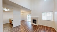 Located at 2300 Riverview Drive in Madera, CA, this two-story, three-bedroom, two-bathroom home offers a well-organized layout across two floors. The main level provides generous living space, highlighted by a soaring vaulted ceiling in the living room that creates an airy, open atmosphere. A tile-surround fireplace serves as the focal point of the living area, complemented by rich hardwood-style flooring that extends throughout the main level. Sliding glass doors lead directly to a covered patio, offering a seamless indoor-outdoor connection with views of the surrounding greenery. The combined dining room and kitchen area features a peninsula with bar seating, warm oak cabinetry, and included appliances, with an adjacent pantry for added storage convenience. A dedicated laundry area and multiple hallway closets enhance practical functionality. Upstairs, three bedrooms are carpeted for comfort, each offering closet space. The spacious primary bedroom provides a private retreat. Two full bathrooms, each with a tub-shower combination and hardwood-style flooring, serve the home. A balcony accessible from the upper level adds additional outdoor space. The home's clean white walls and neutral palette throughout create a bright, versatile interior.