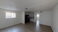 This single-floor unit offers a straightforward, functional layout with an open-concept living and dining area that flows directly into the kitchen. Light wood-tone vinyl plank flooring runs throughout the main living spaces, providing a clean, cohesive look, while textured popcorn ceilings are present throughout. The living area is bright and open, receiving natural light through a window fitted with vertical blinds, and features flush-mount ceiling lighting.

The kitchen is partially open to the living space and is equipped with white cabinetry, dark laminate countertops, and a full suite of black appliances including a refrigerator, electric range, and over-the-range microwave. A single-basin sink sits beneath an additional window, adding natural light to the workspace.

A separate bedroom offers a quiet, neutral environment with its own window fitted with vertical blinds, wood-tone flooring, and a flush-mount light fixture. The bathroom is accessible from the hallway and includes a tub and shower combination, toilet, and vanity with white cabinetry and a dark countertop. The overall aesthetic of the unit is clean and minimal, with white walls throughout.