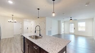 Located at 1025 Retreat Dr. in Bartow, Florida, this well-appointed single-story home offers four bedrooms and three bathrooms within a thoughtfully designed open-concept floor plan. The heart of the home is a modern kitchen featuring rich dark-wood cabinetry extending to the ceiling, stainless steel appliances including a French door refrigerator, electric range, and built-in microwave. A large center island with striking granite countertops and a sleek matte black pull-down faucet serves as both a functional workspace and a natural gathering point. Pendant lighting above the island adds a stylish touch, while the layout flows seamlessly into the dining and living areas, which are brightened by natural light and finished with durable wood-look flooring and a ceiling fan. The bedrooms are carpeted for comfort, with the generously sized primary suite offering ample space and its own closet. Three additional walk-in and standard closets provide plentiful storage throughout. A dedicated laundry room houses full-size washer and dryer units with overhead wire shelving. Light-toned wood-look flooring runs through the main living areas and hallways, while crisp white walls and clean architectural lines create a bright, cohesive aesthetic throughout the entire home.