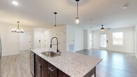 Located at 1025 Retreat Dr. in Bartow, Florida, this well-appointed single-story home offers four bedrooms and three bathrooms within a thoughtfully designed open-concept floor plan. The heart of the home is a modern kitchen featuring rich dark-wood cabinetry extending to the ceiling, stainless steel appliances including a French door refrigerator, electric range, and built-in microwave. A large center island with striking granite countertops and a sleek matte black pull-down faucet serves as both a functional workspace and a natural gathering point. Pendant lighting above the island adds a stylish touch, while the layout flows seamlessly into the dining and living areas, which are brightened by natural light and finished with durable wood-look flooring and a ceiling fan. The bedrooms are carpeted for comfort, with the generously sized primary suite offering ample space and its own closet. Three additional walk-in and standard closets provide plentiful storage throughout. A dedicated laundry room houses full-size washer and dryer units with overhead wire shelving. Light-toned wood-look flooring runs through the main living areas and hallways, while crisp white walls and clean architectural lines create a bright, cohesive aesthetic throughout the entire home.