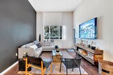 Located at 1901 East 1st Street in Santa Ana, CA, this modern 2-bedroom, 2-bathroom residence offers a thoughtfully designed open-concept layout with striking architectural details throughout. Soaring ceilings define the main living area, where the kitchen flows seamlessly into the living space, creating an airy, expansive feel. The kitchen is appointed with stainless steel appliances — including a gas range, built-in microwave, refrigerator, and dishwasher — complemented by two-tone cabinetry in white and gray, white quartz countertops, a peninsula with pendant lighting, and wood-style flooring. A bold navy accent wall anchors the living area, which benefits from large windows that invite generous natural light. The primary bedroom features soaring ceilings, plush carpeting, tall windows with sheer draping, a walk-in closet, and an ensuite bath with dual sinks, gray cabinetry, and a shower-tub combination. The second bedroom offers flexible use as a home office or guest room. Both bathrooms are well-appointed with wood-style flooring and clean, contemporary finishes. The residence also provides access to a landscaped courtyard with mature trees, manicured greenery, and private outdoor seating — a serene retreat in a vibrant Southern California setting.
