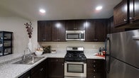 This single-floor residence offers a thoughtfully designed layout that seamlessly connects living, dining, and kitchen spaces. The kitchen is a standout feature, showcasing rich dark-espresso cabinetry with brushed nickel hardware, light granite countertops, and a full suite of stainless steel appliances including a gas range, over-the-range microwave, and refrigerator. Recessed lighting illuminates the workspace, while ample upper and lower cabinetry provides generous storage throughout.

The open-concept living and dining area is warm and inviting, with neutral-toned walls and recessed ceiling lights that create a bright, welcoming ambiance. The living space comfortably accommodates a sofa and coffee table arrangement, complemented by framed wall art that adds a refined, curated feel. A stylish open shelving unit serves as a natural divider between the living and dining zones. The dining area flows directly into the kitchen, making the space ideal for both everyday living and entertaining. Light wood-toned flooring ties the common areas together cohesively, contributing to the overall modern and comfortable character of this well-finished residence.