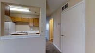 This two-story residential space offers a practical and straightforward layout designed for comfortable everyday living. A defining feature is the pass-through kitchen opening, which connects the kitchen to the adjacent living or dining area, promoting an open flow between spaces. The kitchen is equipped with warm-toned wooden cabinetry providing ample storage, a built-in sink, and overhead fluorescent lighting that brightens the workspace. A textured ceiling is visible throughout, adding subtle visual character to the interior.

The hallway, finished with neutral-toned carpet, extends toward additional rooms, including what appears to be a well-lit room visible at the corridor's end. White painted walls and white baseboards create a clean, consistent aesthetic throughout. Overhead HVAC vents are integrated into the ceiling, ensuring climate control across the space. A thermostat panel is mounted along the hallway wall for easy access. Doors along the corridor lead to additional rooms, suggesting a multi-room floor plan spread across two levels. The overall ambiance is functional and neutral, offering a versatile canvas for personalization.
