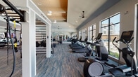 Located at Avalon Point in Missouri City, Texas, this single-story fitness center is designed to support a comprehensive workout experience across several distinct zones. The facility opens into a welcoming entry area finished with large-format tile flooring, a built-in teal storage console, a textured accent wall, and vaulted ceilings that establish an airy, modern aesthetic throughout.

The cardio zone runs along a wall of oversized black-framed windows, offering direct views of the outdoor pool area and surrounding palm-lined courtyard. Treadmills, ellipticals, and stair climbers are arranged to take full advantage of this natural light and scenery. Ceiling fans overhead contribute to a comfortable environment during high-intensity sessions.

An adjacent strength training area features cable machines, Smith machines, free weights, and a heavy-duty tire for functional training. Floor-to-ceiling mirrors line the walls, enhancing the sense of space and allowing for proper form monitoring. The high ceilings in this zone add to the open, professional atmosphere.

A separate spin studio houses a row of cycling bikes arranged before a large display screen and full-wall mirrors, with windows on multiple sides bringing in additional natural light. Plio boxes and auxiliary equipment are neatly stored near the entry, completing this fully appointed fitness facility.