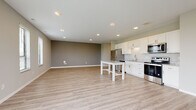 This contemporary single-floor unit offers a thoughtfully designed open-concept layout that seamlessly connects the living area and kitchen. Light wood-tone luxury vinyl plank flooring flows throughout the main living spaces, complemented by neutral warm-gray walls and crisp white trim, creating a clean and inviting aesthetic. Recessed lighting throughout ensures consistent illumination across the space.

The kitchen is well-appointed with white shaker-style cabinetry, granite countertops, a subway tile backsplash, and a full suite of stainless steel appliances including a refrigerator, electric range, and over-the-range microwave. A central kitchen island with a white base and granite top provides additional prep and dining space.

The expansive living area is bathed in natural light, courtesy of multiple windows fitted with horizontal blinds and a large sliding glass door that opens to outdoor views of a green landscape. The open floor plan provides generous room for a variety of furniture arrangements.

The bedroom features plush patterned carpeting and a window with views of the surrounding greenery, offering a quiet and comfortable retreat. The bathroom is finished with a white vanity featuring granite countertops, brushed nickel hardware, a large mirror, and a tall linen storage cabinet, all set atop matching luxury vinyl plank flooring.