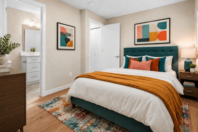 A stylish and comfortable bedroom with vibrant accents, warm wood-style flooring, and convenient access to the adjoining bathroom. - Crossroads at Meridian Apartments