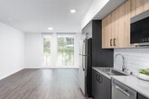 This well-appointed single-floor unit offers a thoughtfully designed layout with contemporary finishes throughout. The open-concept living and kitchen area is bright and airy, highlighted by large windows that invite abundant natural light and offer outdoor views. The kitchen is outfitted with a sleek combination of dark and warm wood-toned cabinetry, stainless steel appliances including a full-size refrigerator and dishwasher, a subway tile backsplash, and light countertops — creating a functional yet visually striking space. Wood-look flooring flows consistently throughout the unit, lending a sense of warmth and cohesion. The bedroom is generously proportioned, featuring floor-to-ceiling windows that fill the room with daylight and views of the surrounding greenery. The bathroom is finished with elegant marble-style tile surround in the tub and shower area, complemented by a dark-toned vanity and wood-look tile flooring. Near the entryway, a dedicated nook houses a stacked washer and dryer, providing convenient in-unit laundry. An additional flexible room with rich hardwood-style flooring offers further utility. Clean white walls, recessed lighting, and a minimalist aesthetic give the unit a modern, move-in-ready appeal throughout.