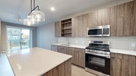Located at 365 S Moorland Rd in Brookfield, WI, this one-bedroom, one-bathroom unit offers a thoughtfully designed layout with modern finishes throughout. The kitchen is a standout feature, showcasing wood-tone flat-panel cabinetry, open shelving, a white quartz countertop, full-tile backsplash, and a suite of stainless steel appliances including a gas range, microwave, dishwasher, and refrigerator. A large center island with pendant lighting provides additional prep space and casual seating. Light-toned hardwood-style flooring runs throughout the main living area, enhancing the bright, open atmosphere. The bedroom is carpeted for comfort and features a generously sized window that brings in natural light and views of the surrounding community. Four closets provide ample storage throughout the unit. The bathroom is clean and contemporary, featuring a tub and shower combo with white subway tile surround and chrome fixtures. A private balcony extends the living space outdoors, offering views of the landscaped courtyard and community pool below. The building's modern exterior features mixed metal panel cladding with bold accent colors, reflecting a contemporary architectural aesthetic.
