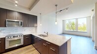 Located at 7911 Westpark Dr in McLean, VA, this well-appointed one-bedroom, one-bathroom residence offers a thoughtfully designed open-concept layout across a single floor. The contemporary kitchen serves as a central hub, showcasing dark espresso cabinetry, granite countertop surfaces, a tile backsplash, stainless steel appliances including a range, microwave, and refrigerator, and a peninsula island with an undermount sink and pendant lighting overhead. Track lighting and a tray ceiling detail add architectural dimension to this space. Wood-look flooring flows throughout the main living areas, connecting the kitchen seamlessly to the living room, which is bathed in natural light from large floor-to-ceiling windows framing lush treetop and skyline views. The generously sized bedroom features plush carpeting, a ceiling fan, access to a private balcony, and expansive windows that continue the theme of abundant natural light and outdoor views. The bathroom is finished with neutral tile flooring and a tub-shower combination with brushed hardware. The entryway provides a welcoming transition into the home with hardwood-style flooring and interior closet access. This residence combines modern finishes with a bright, airy ambiance in a desirable McLean location.